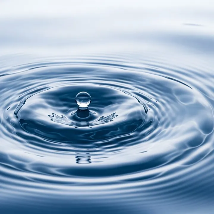 A single water drop rippling across a still blue surface